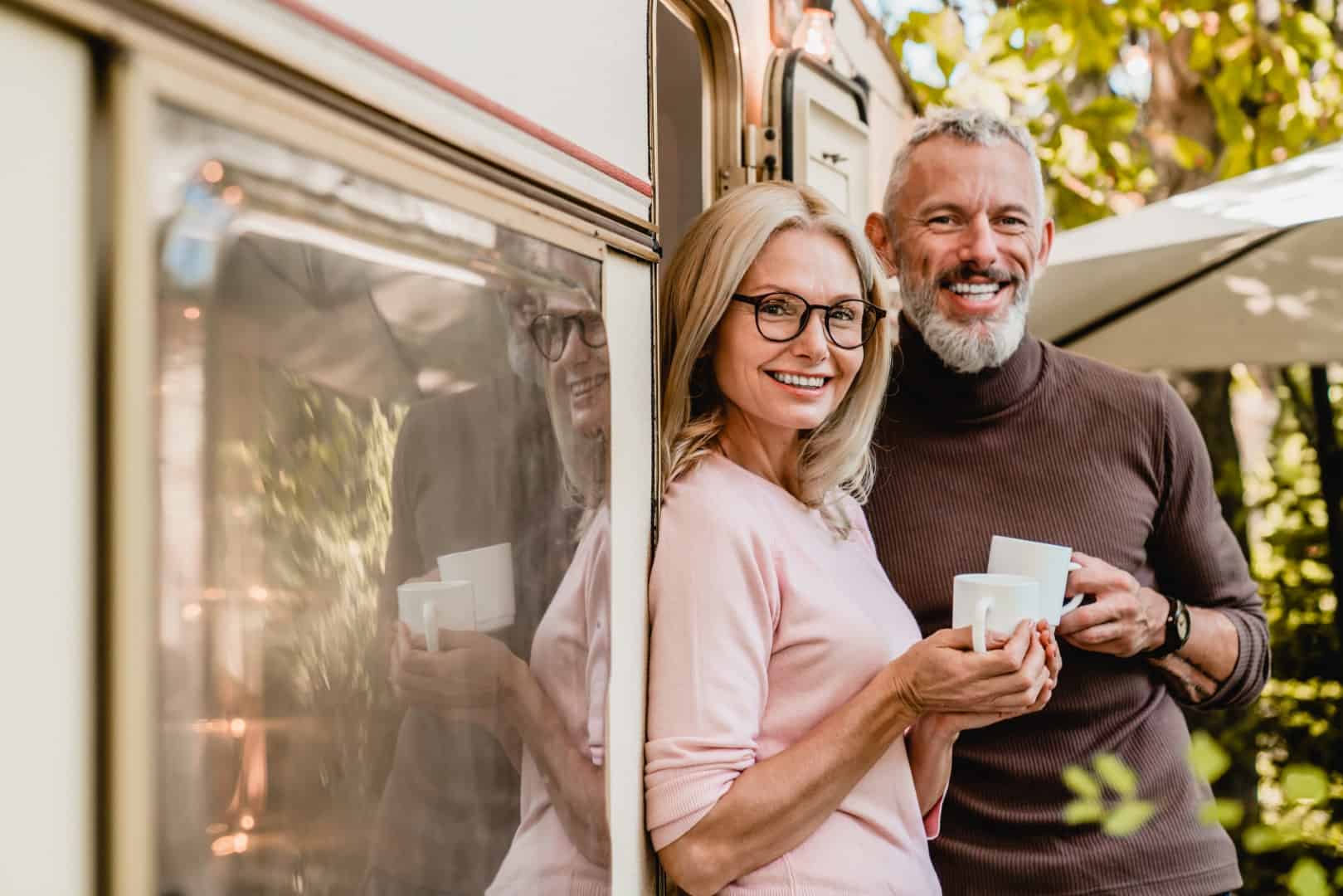 Portrait of happy successful mature couple smiling at the camera holding cups of coffee near their van